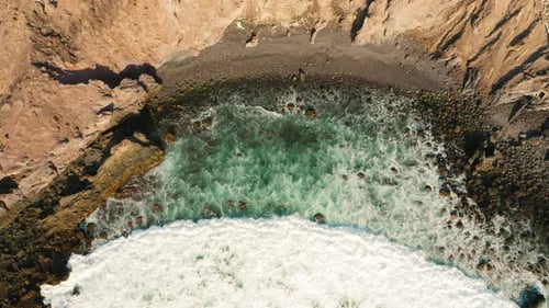 Zusammenfassung: Breite, schäumende Meereswellen stürzen auf Felsen und smaragdblaues Wasser dringt mit dem Meer in die Bucht