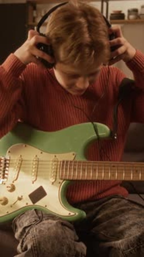 Vertical Boy Playing Guitar at Home and Putting on Headphones