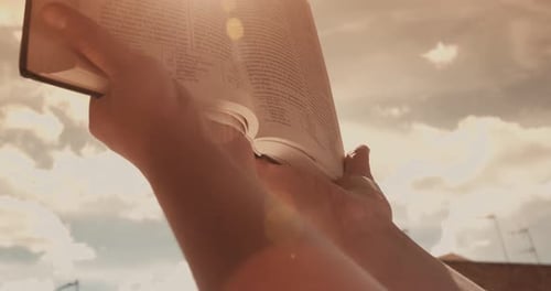 Woman Holding A Bible Against A Sunny Blue Sky