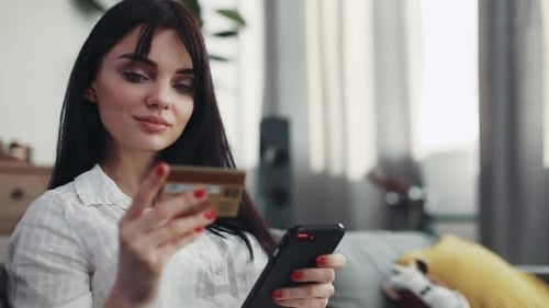Young Woman Using Phone and Credit Card Indoors