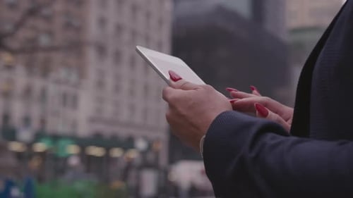 A woman scrolls on a tablet on a city sidewalk
