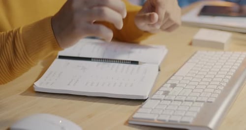 Closeup of Male Hand Working with Computer and Writing in Notebook at Office Desk in Evening