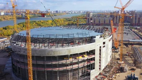Edificio de estadio deportivo con grúas de torre alta en la orilla del río
