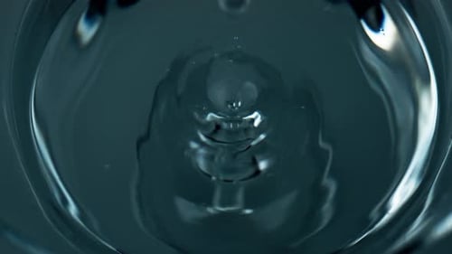 Refreshing water droplet falls waving into a transparent glass cup top view