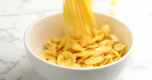Cornflakes Pouring into Bowl on Marble Surface