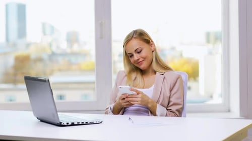 Smiling businesswoman texting a message on her smartphone in the office