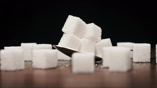 Ein Stapel von Zuckerwürfeln im Löffel wird auf dem Tisch auf schwarzem Hintergrund gedreht. Nahaufnahme