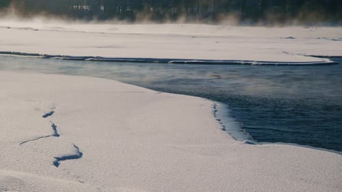 A Beautiful and Tranquil Winter Landscape Featuring a SnowCovered River with a Frosty Edge Alongside