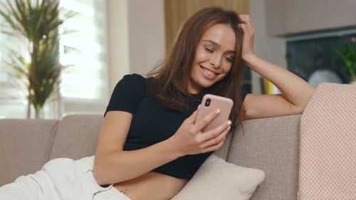 Close Up Young Woman Sitting on Sofa and Using Smartphone in Modern Room Feel Happy Smiling Internet