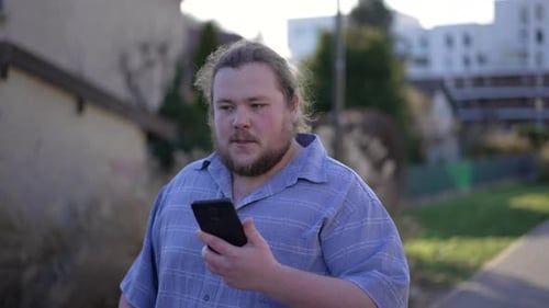 Young man receiving negative news on cellphone device while walking outdoors in city street.