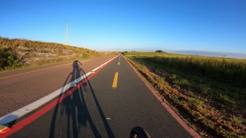 Schatten eines Radfahrers, der an einem sonnigen Tag auf dem Radweg fährt, POV-Aufnahme