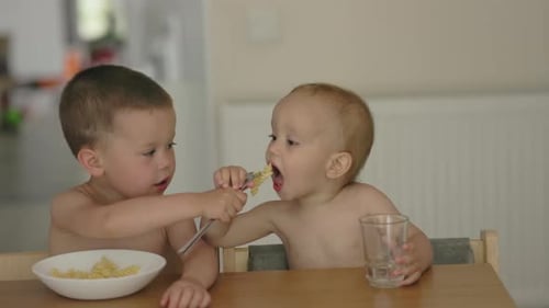 Child Feeds Pasta to Infant at Table