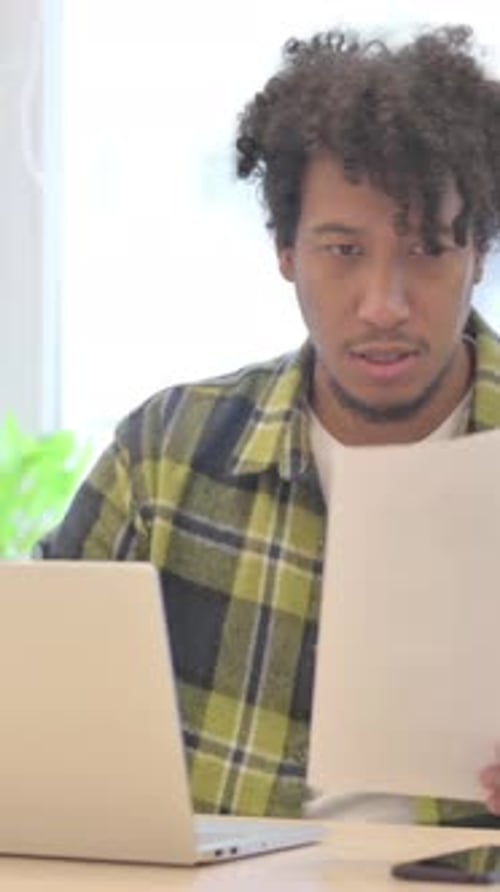 Young Man Working on Laptop with Documents Indoors