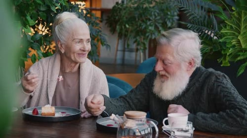 Laughing Elderly Lady Telling Story to Husband while Enjoying Cake in Cafe