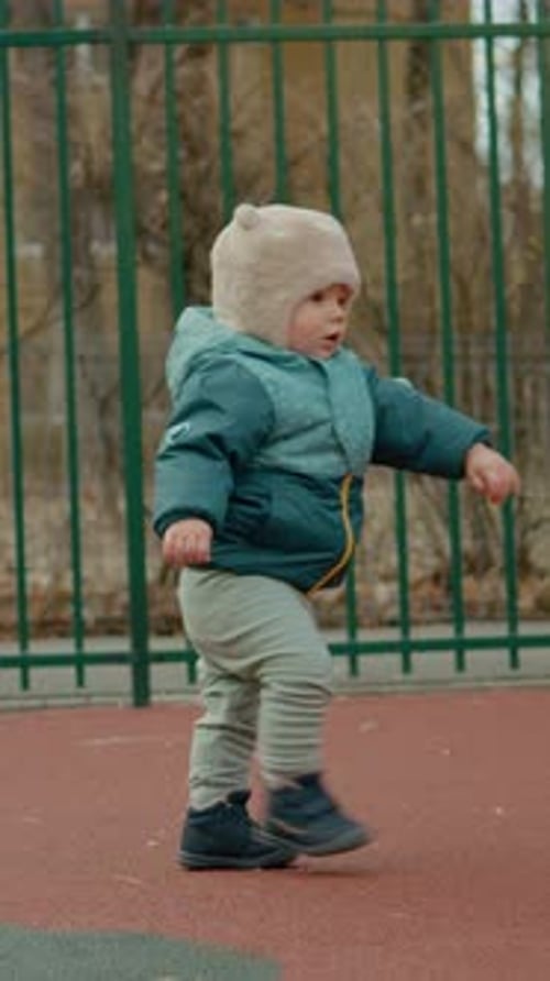 Vertical video Baby explores playground while taking first steps in a joyful