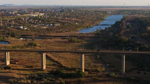 Aerial shot showing multiple cars driving on a big viaduct in sunlight, city near lake in the backgr