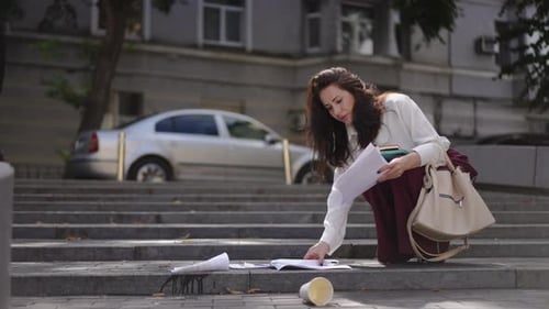 A Man in a Suit Helps a Businesswoman Collect Documents That Have Fallen From Her Hands to the