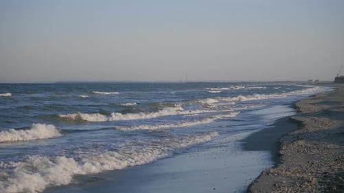 Statische Zeitlupenaufnahme von Wellen, die von links nach rechts auf einem Meer mit blauem Wasser von einem Sandstrand aus gesehen d