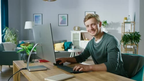 Portrait of the Focused Young Man Working on a Personal Computer while Sitting at His Desk, Smiling