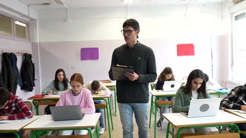 Teacher Supervising Students Working on Laptops in Classroom