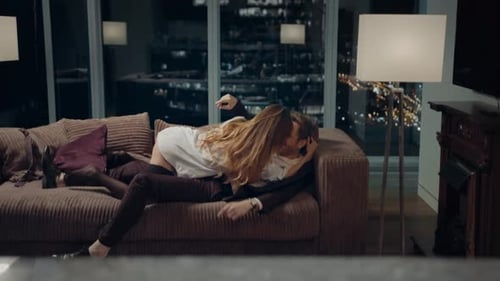 A young girl in a white shirt hugs a man and they lie down on the sofa, a romantic date at home.