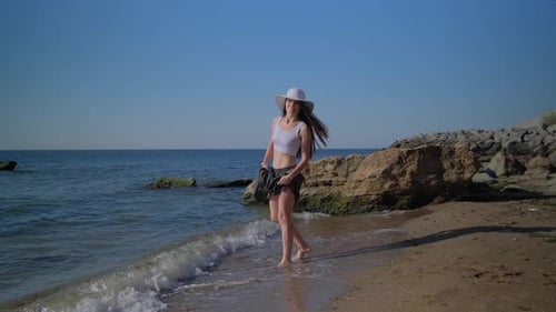 Young Pretty Lady In Beachwear Walks In Shallow Water On The Seashore