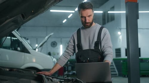 Caucasian Man Mechanic Working in Car Service Workshop Fixing Engine Using Laptop Electronic