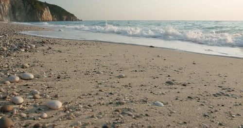 Soft calm foam waves rolling ashore on sandy beach of Mediterranean sea in golden sunset evening sun