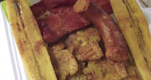 primer plano de un plato peruano de patacones, plátano maduro frito, cecina y chorizo.