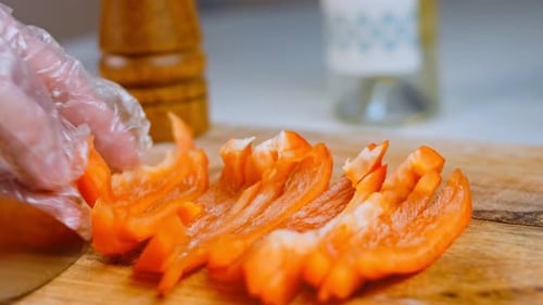 Front View of the Young Chef Cut Thin Slices of a Piece of Red Pepper with a Knife on the Cutting