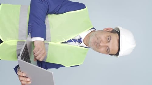 Vertical video of Engineer holding laptop laughing at camera.