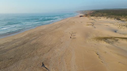 Aerial view of group of horses riding along the shore of Bordeira beach Portugal during sunset light