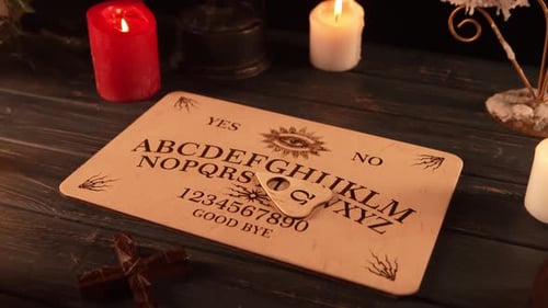 Close Up Video of a Wooden Ouija Board on a Table Surrounded By Candles Candlesticks and Other