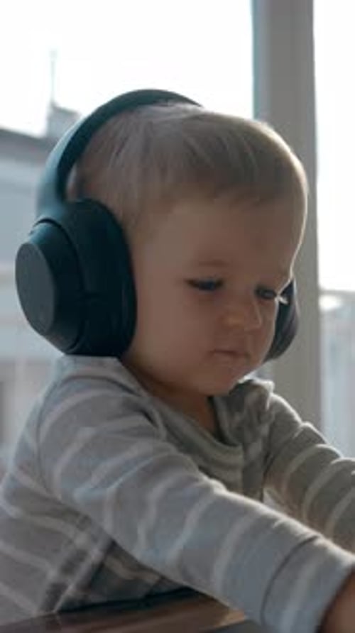 Blonde Baby Wearing Headphones at Table Indoors