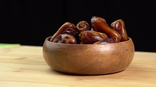 Dates fruits in wooden bowl rotate on wooden background close up, rotation. Eating dried fruits