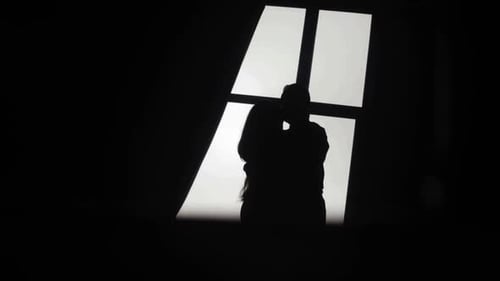 Silhouettes of a couple near the window which is kissing and hugging