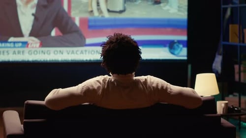 Person Relaxing on Couch Watching VOD Channel on Large Television Set in Living Room