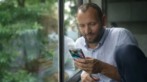 Young Man Using Smartphone Sitting by Window at Home Adult