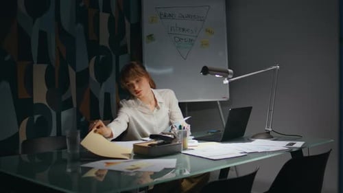Tired Woman Reviews Paperwork at Conference Table