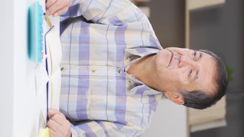 Mature Man Reading a Book Indoors at Desk