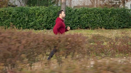 Fit Man Running in a City Park Trail - Tracking shot profile view