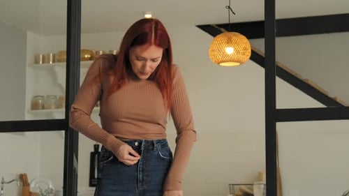 Upset Overweight Mature Woman Trying to Button Up Tight Pants at Home