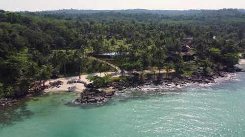 Flying toward a tropical island, with a stunning beach and palm trees. On the island is a charming r