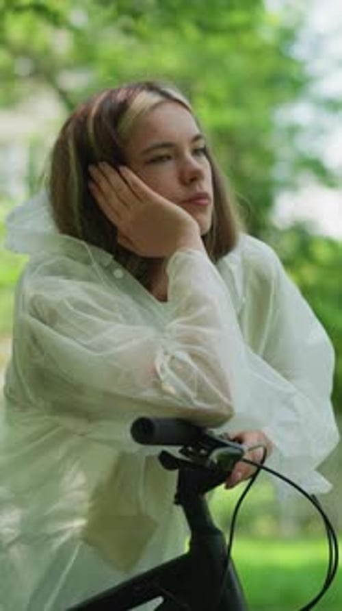 Thoughtful Woman in Raincoat Reflects By Bicycle in Green Forest