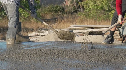 Baubetonarbeiter nivellieren frischen Zement mit Schaufeln auf einer sonnigen Baustelle