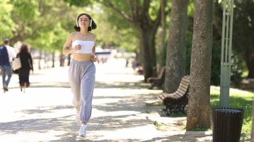 A Woman is Running on a Sidewalk in a Park