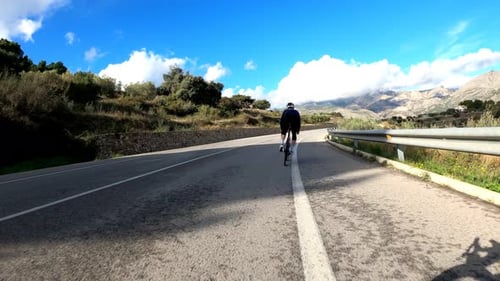 Cyclist riding road bicycle through picturesque mountain canyon at sunny day
