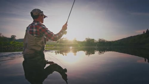 Fly fishing. Angler stands in the river and casts the fly at sunset. Fisherman fishing on fly