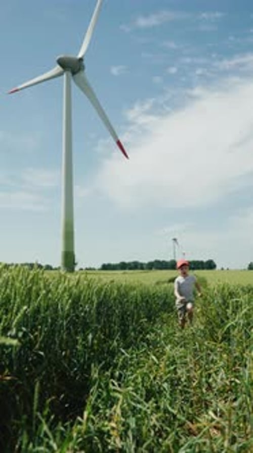Young Boy Running in Green Weat Field with Wind Turbine in the Background