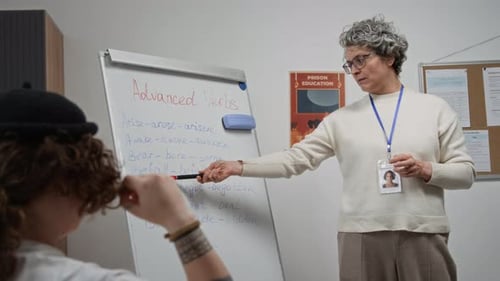 Female Teacher Pointing at Board and Speaking to Inmates during Class in Prison